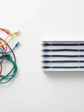 Rommelige kleurrijke ethernetkabels en stroomkabels op wit bureau naast georganiseerde kabelgoot met nette parallelle lijnen