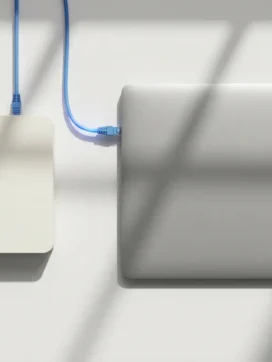 Laptop verbonden met witte router via ethernet kabel op wit bureau met zachte schaduwen en minimalistisch design