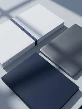 Stapel witte compliance-documenten naast een laptop op een lichtgrijs bureau, met een donkerblauwe map als ankerpunt.