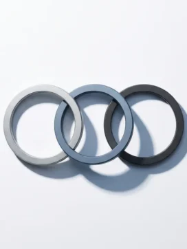 Drie matte stalen ringen aaneengeschakeld op wit oppervlak, middelste ring licht losstaand, geometrische schaduwen in zilver en leisteenblauw.